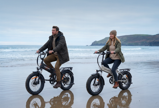 A man and a woman are riding folding electric bicycles to the beach.